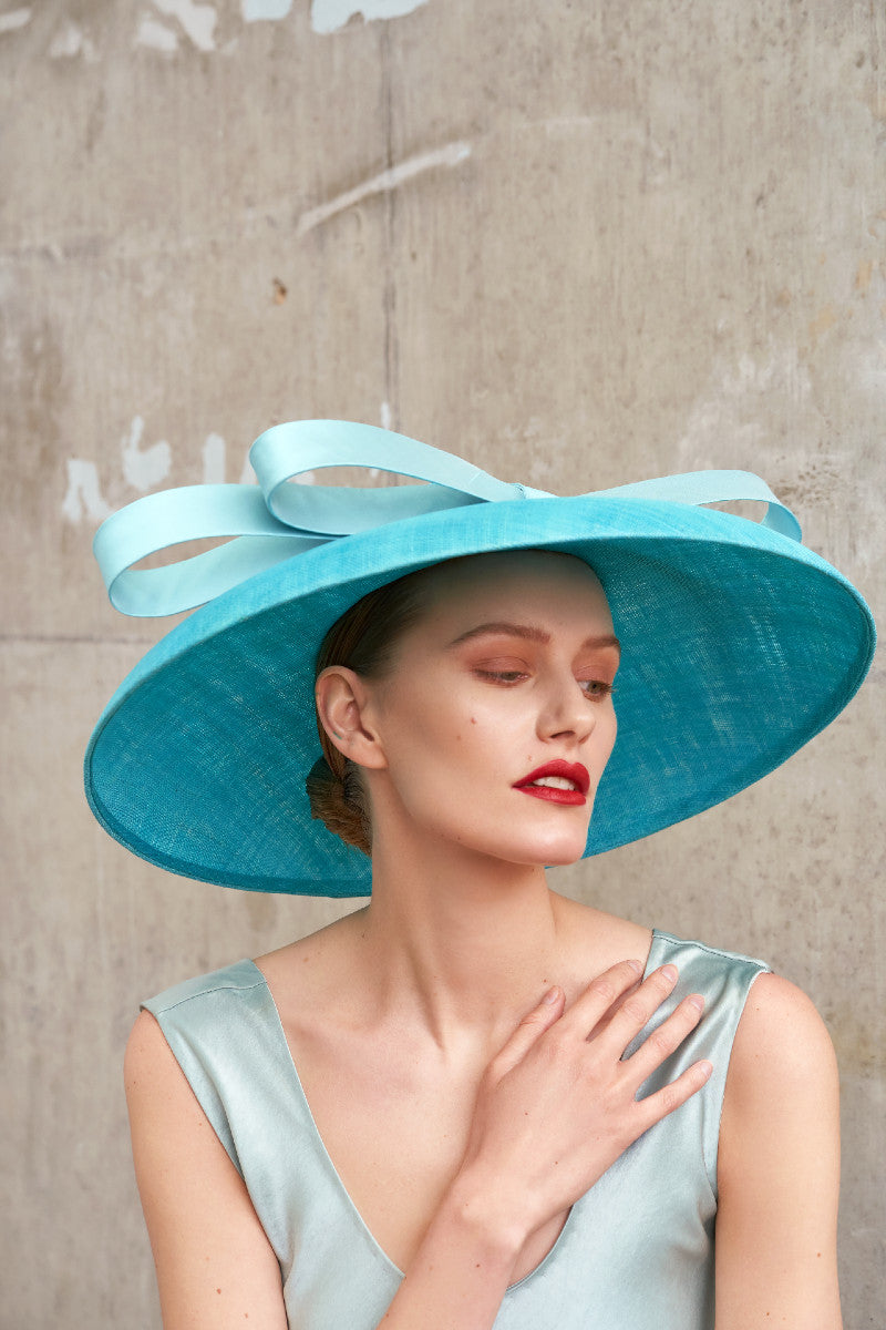 Woman wearing a wide brim turquoise blue sinamay hat with big bow