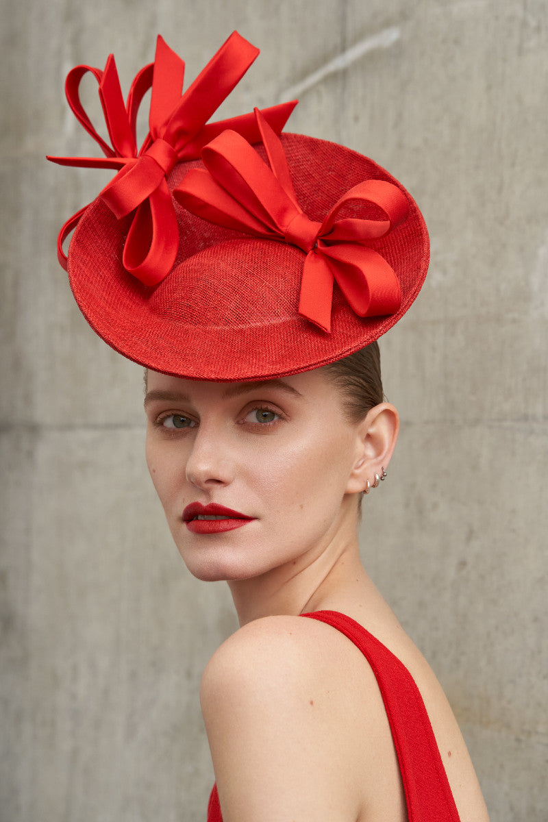 White woman wearing a red saucer hat with two bow on top