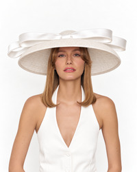 Model wearing the PRISCILLA white wide brim hat with an oversized silk bow, styled with a white halterneck outfit.