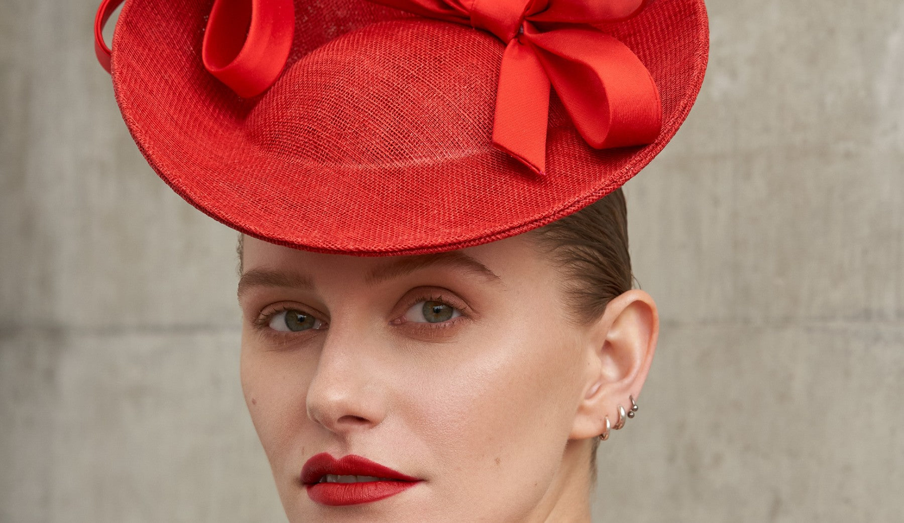 White woman wearing a red saucer hat with two bow on top
