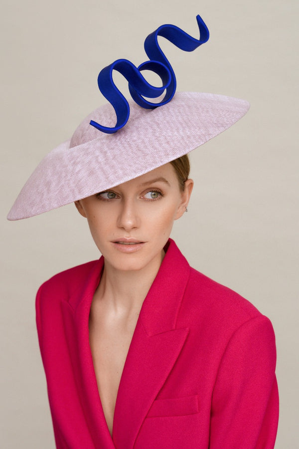 Woman wearing lilac base saucer hat with a shock blue curvy trimming on top